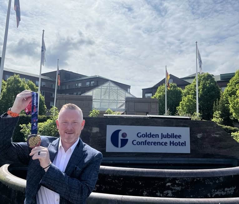 Denis stands in front of Golden Jubilee Conference hotel with medal