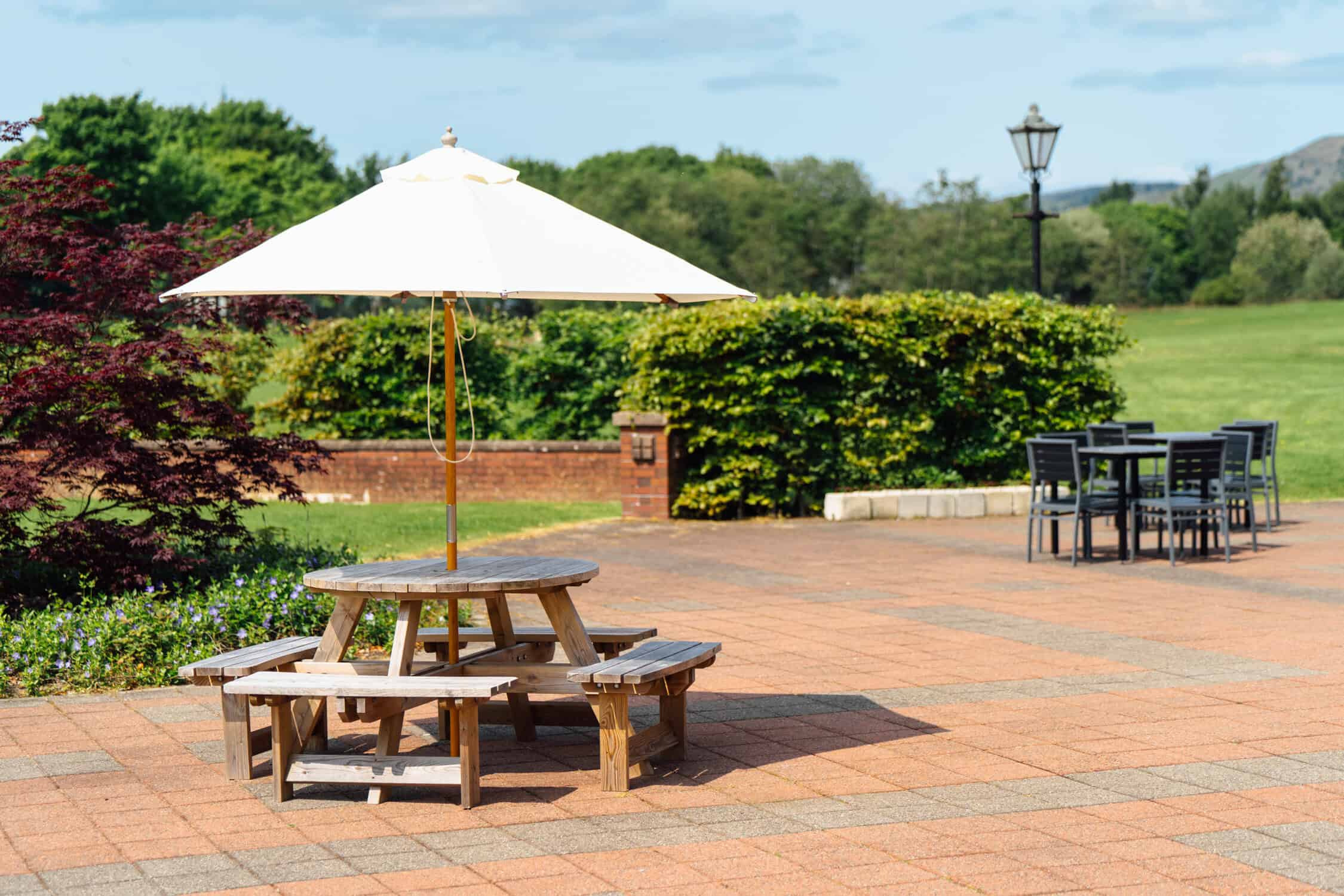 outdoor picture showing a picnic table with umbrella and green grass